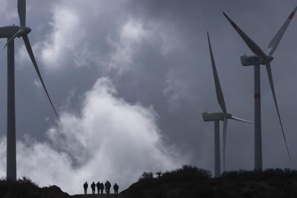 FILE - People walk near wind turbines on a government-sponsored wind farm, inaugurated by Mexican President Felipe Calderon, in La Rumorosa, northern Mexico, March 9, 2010. Mexico’s President Andrés Manuel López Obrador said Wednesday, Feb. 8, 2023 that he expects the U.S. government or U.S. banks to provide interest-free loans to build four wind-power farms in the narrow waist of southern Mexico, an area known as the Isthmus of Tehuantepec. (AP Photo/Guillermo Arias, File)