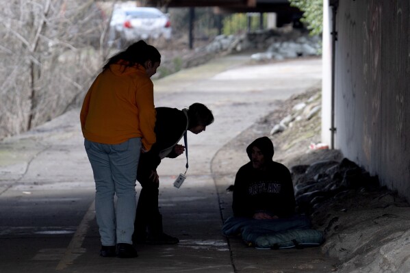 Members of the Resiliency Empowerment Support Team (REST) Letha Croff, left, and Torie Baxter, second from left, talk to a homeless person sleeping under a bridge in Chico, Calif., Feb. 8, 2024. A measure aimed at transforming how California spends money on mental health will go before voters in March as the state continues to grapple an unabated homelessness crisis. The REST Program does daily visits to homeless encampments to get them into treatment or housing. Butte County officials fear the REST program would lose its funding if California voters approve Proposition 1 (APPhoto/Rich Pedroncelli)