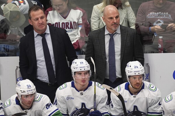 Vancouver Canucks assistant coach Adam Foote, back left, and head coach Rick Tocchet look on from the team box in the third period of an NHL hockey game against the Colorado Avalanche, April 10, 2025, in Denver. (AP Photo/David Zalubowski, file)