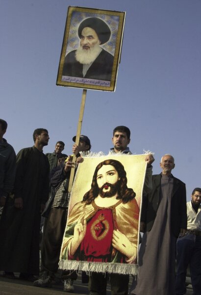 FILE - In this Jan. 19, 2004 file photo, an Iraqi Christian holds a carpet with an image of Jesus Christ and a poster of Grand Ayatollah Ali al-Husseini al-Sistani during a march in Baghdad, Iraq. On Saturday, March 6, 2021, Pope Francis will visit the 90-year-old Grand Ayatollah who is revered by many Shiites worldwide and whose words hold powerful influence in Iraq and beyond. The pontiff and ayatollah will meet in al-Sistani’s modest home in the Iraqi city of Najaf. (AP Photo/Hadi Mizban, File)