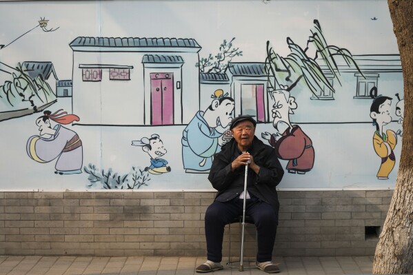 An elderly man sits in front of a mural depicting traditional China in Beijing, China, Friday, April 12, 2024. (AP Photo/Tatan Syuflana)