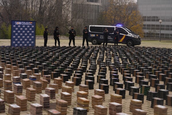 Police officers stand by part of a haul of 11 tons of cocaine, displayed in the patio of a police station in Madrid, Spain, Tuesday, Dec. 12, 2023. Spanish authorities say that they have confiscated 11 tons of cocaine and arrested 20 people in two different operations against the smuggling of the illegal drugs inside shipping containers. Investigators believe that the criminal organization was using a frozen seafood company as a front to bring the drug from South America. (AP Photo/Paul White)