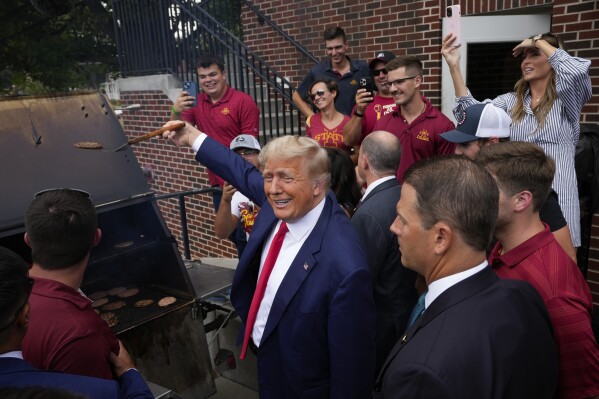 Former President Donald Trump holds a spatula with a hamburger on it as he works the grill during a stop at the Alpha Gamma Rho, agricultural fraternity, at Iowa State University before an NCAA college football game between Iowa State and Iowa, Saturday, Sept. 9, 2023, in Ames, Iowa. (AP Photo/Charlie Neibergall)