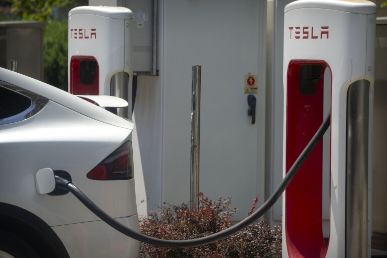 FILE - A vehicle charges at an electric vehicle station outside of a Tesla dealership in Beijing, June 24, 2023. Amid an ongoing push to make transportation less damaging to the climate, electrification continued to accelerate in 2023, with one in five cars sold across the globe this year expected to be electric, according to the International Energy Industry. (AP Photo/Mark Schiefelbein, File)