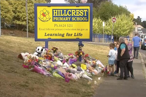 In this image made from video, people lay flowers at a makeshift memorial outside the Hillcrest Primary School in Devonport, Tasmania, Australia, Friday, Dec. 17, 2021. Local residents on Friday placed floral tributes outside the Australian school where five children died after falling from a bouncy castle that was lifted into the air by a gust of wind. (Channel 9 via AP)