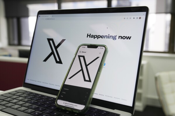 The opening page of X is displayed on a computer and phone in Sydney, Monday, Oct. 16, 2023. Australia's online safety watchdog has fined X, formerly known as Twitter, $385,000 for failing to explain how it tackles child sexual exploitation on the social media platform. (AP Photo/Rick Rycroft)