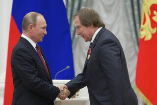 FILE - Russian President Vladimir Putin, left, presents a medal to Russian cellist Sergei Roldugin, during an awarding ceremony in Moscow's Kremlin, Russia, on Thursday, Sept. 22, 2016. Four former bankers with the now-shuttered Swiss affiliate of a major Russian bank have gone on trial over allegations that they didn't properly check accounts opened in the name of a Russian cellist with longtime ties to President Vladimir Putin. (AP Photo/Ivan Sekretarev, Pool, File)