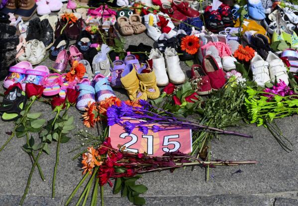 Flowers, children's shoes and other items rest at a memorial at the Eternal flame on Parliament Hill in Ottawa on Tuesday, June 1, 2021, in recognition of discovery of children's remains at the site of a former residential school in Kamloops, British Columbia. (Sean Kilpatrick/The Canadian Press via AP)