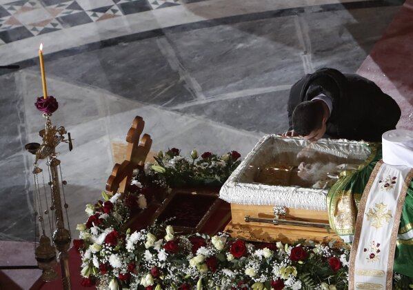 In this photo taken Saturday, Nov. 21, 2020, a man kisses the coffin of Patriarch Irinej as he lies in repose at the St. Sava Temple in Belgrade, Serbia. After the two most senior Serbian Orthodox Church leaders died within a month after testing positive with the coronavirus, health experts and even hardcore believers are starting to worry. The spread of the virus within the largest religious group in the Balkans is getting more alarming by the day. (AP Photo/Darko Vojinovic)