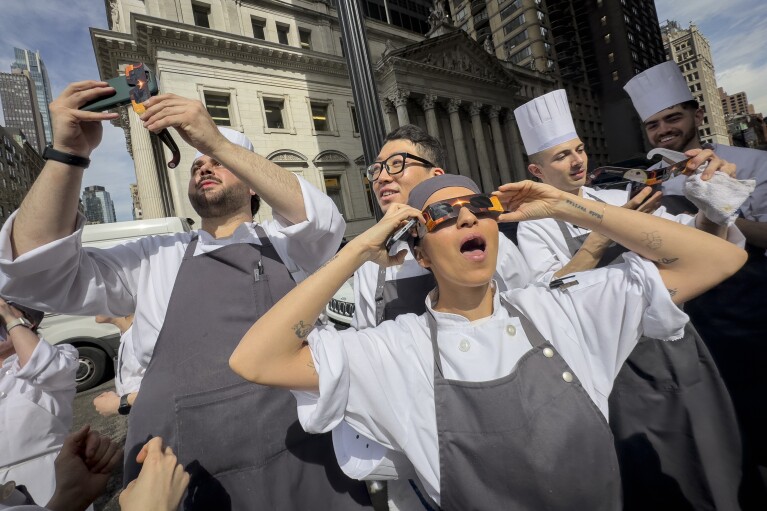 عمال المطاعم في منطقة فلاتيرون في مانهاتن يأخذون استراحة لمشاهدة كسوف الشمس، الاثنين 8 أبريل 2024، في نيويورك. (صورة AP / جون مينشيلو)