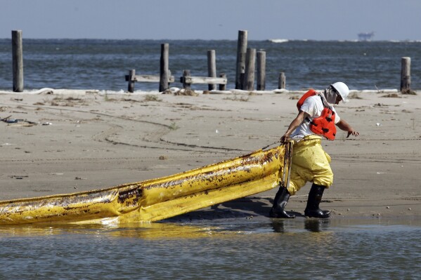 文件-2010年5月22日，路易斯安那州格兰德岛卡米纳达山口，一名工人正在拉动一个被水流固定在码头上的石油繁荣。当一次致命的爆炸摧毁了英国石油公司在墨西哥湾的深水地平线钻井平台时，成千上万的普通民众被雇佣来帮助清理环境破坏。这些工人在沿着海岸线捡起焦油球、在渔船上铺设拦油栅以吸收浮油以及营救油污覆盖的鸟类时，接触到原油和化学分散剂Corexit。（美联社照片/Patrick Semansky，文件）