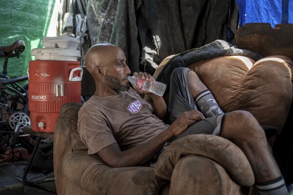 Stefon James Dewitt Livengood drinks water in his tent where he lives in Phoenix on Sunday, July 23, 2023. Livengood is experiencing homelessness while living through a record breaking heat wave. (AP Photo/Thomas Machowicz)