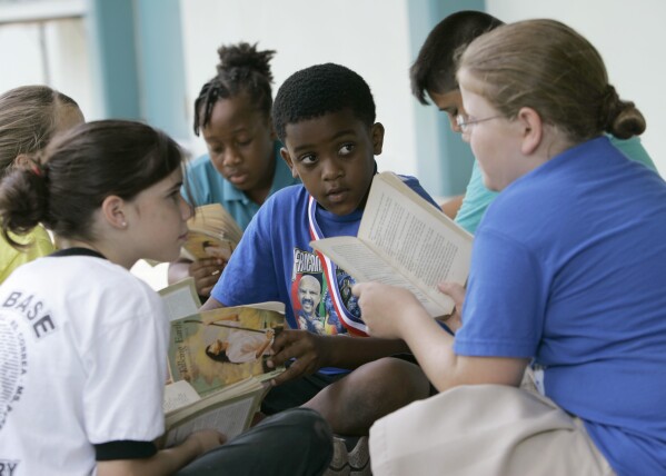 FILE - Joseph Webb, center; Kristina Carr, right; and Kaelyn Korovich, left, read outside their classroom at Air Base Elementary School, June 4, 2009, in Homestead, Fla. The school was one of the first in Miami-Dade County to integrate Black students. Friday, May 17, 2024, marks 70 years since the U.S. Supreme Court ruled that separating children in schools by race was unconstitutional. On paper, Brown v. Board of Education still stands. In reality, school integration is all but gone, the victim of a gradual series of court cases that slowly eroded it, leaving little behind. (AP Photo/Wilfredo Lee, File)