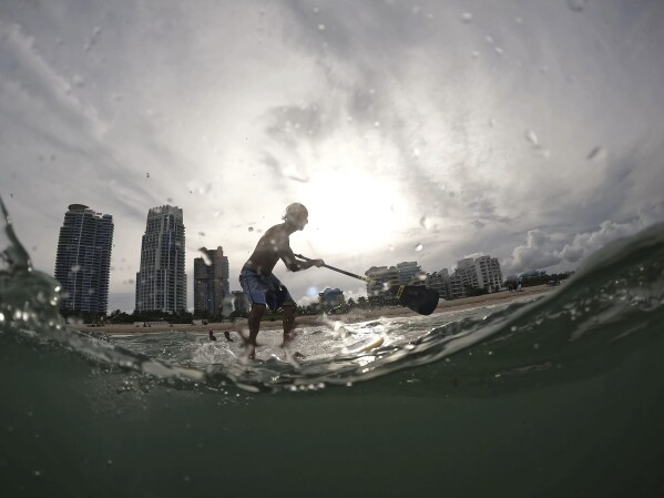 Graziano La Grasta, a local contractor and paddle board enthusiast, rides a small wave off South Beach, Friday, July 28, 2023, in Miami Beach, Fla. Humans naturally look to water for a chance to refresh, but when water temperatures get too high, some of the appeal is lost. (APPhoto/Rebecca Blackwell)