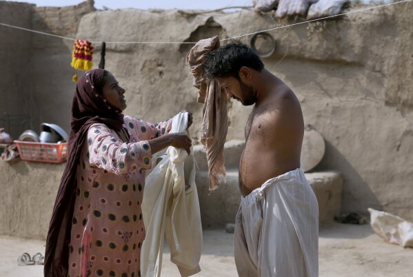 Rizia Bibi, left, helps his son Mohammad Ikram, who play snooker with his chin, to wear long shirt at their home in a village near Samundri town, Pakistan, Sunday, Oct. 25, 2020. Ikram, 32, was born without arms, but everyone simply admires his snooker skills when he hits the cue ball with his chin and pots a colored ball on a snooker table. He lives in a remote rural town of Punjab province and his physical disability doesn't come in his way to fulfill his childhood dream of playing the game of snooker. (AP Photo/Anjum Naveed)
