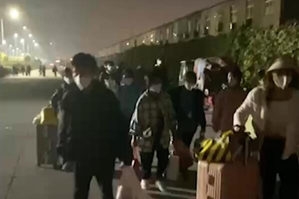 In this photo taken from video footage and released by Hangpai Xingyang, people with suitcases and bags are seen leaving from a Foxconn compound in Zhengzhou in central China's Henan Province on Saturday, Oct. 29, 2022. Workers in a Foxconn facility in the central Chinese city of Zhengzhou appear to have left the facility to avoid COVID-19 curbs, with many traveling by foot days after an unknown number of factory workers were quarantined in the facility following a virus outbreak. (Hangpai Xingyang via AP)