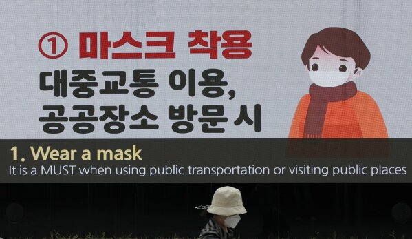 A woman wearing a face mask passes by a screen showing precautions against the coronavirus at the Dongdaemun Design Plaza in Seoul, South Korea, Sunday, April 19, 2020. South Korea's prime minister says the country will maintain much of its social distancing guidelines until May 5 but will relax some limits. (AP Photo/Lee Jin-man)