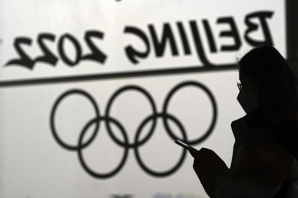 FILE - A woman looks at her phone as she passes an Olympic logo inside the main media center for the 2022 Winter Olympics, Jan. 18, 2022, in Beijing. (AP Photo/David J. Phillip, File)