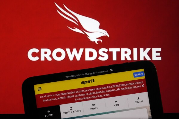 The logo for CrowdStrike and a Spirit Airlines webpage are shown on a computer screen and mobile phone screen, in New York, Friday, July 19, 2024. (AP Photo/Richard Drew)