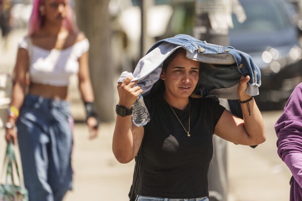 FILE - Sorelly Restrepo, of Colombia, shields herself from the sunlight in the Little Tokyo district of Los Angeles, July 27, 2023. Across the U.S., many people are living through one of the most brutal summers of their lives and reckoning with the idea that climate change is only going to make matters worse in the coming decades. (AP Photo/Damian Dovarganes, File)