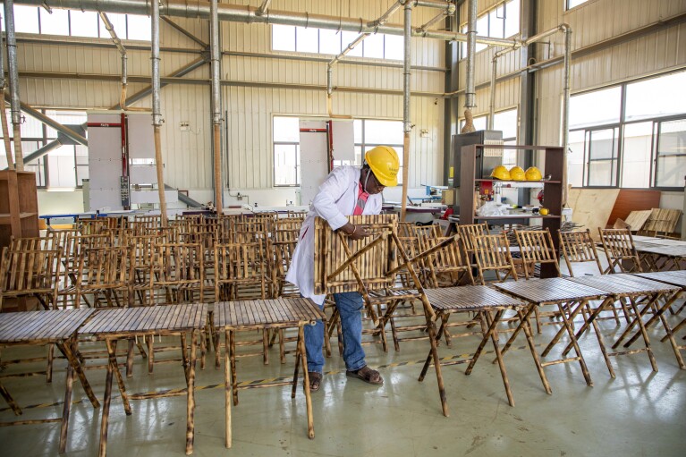 Taga Nuwagaba, a bamboo farmer and businessman who owns a bamboo furniture factory, holds a piece of furniture in Wakiso, Uganda on March 13, 2024. Bamboo farming is on the rise in Uganda, where the hardy and fast-growing crop is seen by the government as having real growth potential. Businesses can turn it into furniture and other products. (AP Photo/Dipak Moses)