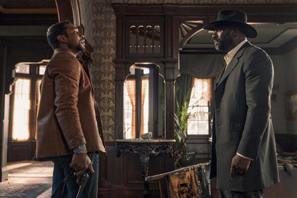 This image released by Netflix shows Jonathan Majors, left, and Idris Elba in a scene from "The Harder They Fall." (David Lee via AP)