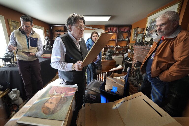Appraiser Kaja Veilleux examines a painting brought in by Wanda Morris, background, and her husband, Jeff Morris, right, while associate appraiser Darrin Guitreau, left, takes notes, at Thomaston Place Auction Galleries, Tuesday, Nov. 19, 2024, in Thomaston, Maine. (AP Photo/Robert F. Bukaty)