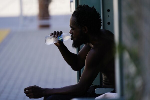 FILE - A person drinks a bottle of water in the shade as temperatures are expected to hit 119-degrees (48.3 Celsius) July 20, 2023, in Phoenix. Earth last year shattered global annual heat records, the European climate agency said Tuesday, Jan. 9, 2024. (AP Photo/Ross D. Franklin, File)