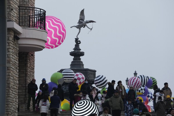 Shoppers gather under a statue of Cupid as they visit a shopping mall in Beijing on Dec. 30, 2023. China’s population dropped by 2 million people in 2023 in the second straight annual drop as births fell and deaths jumped. (AP Photo/Ng Han Guan)