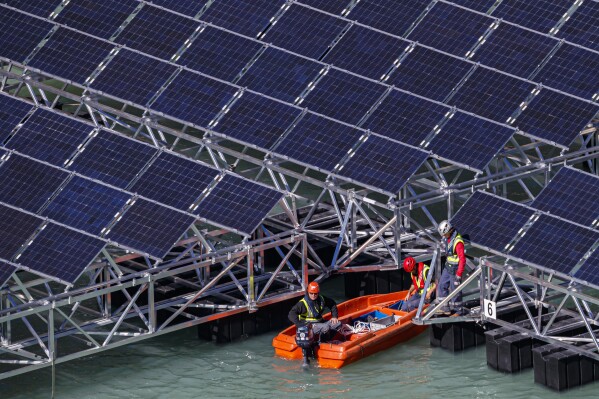 FILE - Workers assemble floating barges with solar panels on the 'Lac des Toules', an alpine reservoir lake, in Bourg-Saint-Pierre, Switzerland, Tuesday, Oct. 8, 2019. Voters in a southern Swiss region cast their ballots Sunday, Sept. 10 2023, to decide whether to allow large solar parks on their sun-baked Alpine mountainsides as part of the federal government’s push to develop renewable energies. (Valentin Flauraud/Keystone via AP, File)