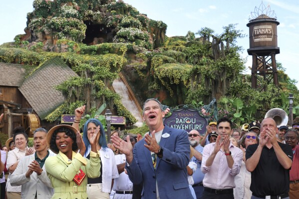 With Princess Tiana, Walt Disney World president Jeff Vahle cheers during a "Thank You Fête" honoring cast members at a preview event for Tiana's Bayou Adventure at the Magic Kingdom in Bay Lake, Fla., Monday, June 10, 2024. The ride —redeveloped from the park's original Splash Mountain— officially opens to Disney guests on June 28. (Joe Burbank/Orlando Sentinel via AP)