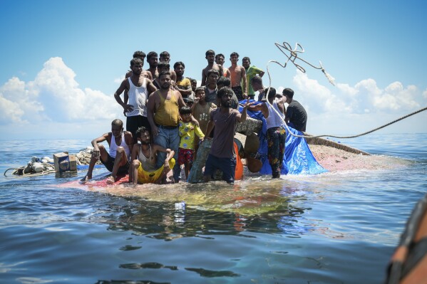 Ethnic Rohingya refugees stand on their capsized boat as rescuers throw a rope to them off West Aceh, Indonesia, on Thursday, March 21, 2024. The wooden fishing boat carried about 140 Rohingya refugees, but only 75 people were rescued. In interviews with The Associated Press, eight of the survivors described abuses on board. (AP Photo/Reza Saifullah)