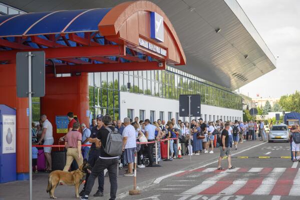 Security personnel and an explosive sniffing dog stand at the entrance of the departures terminal as passengers wait in line at the international airport in Chisinau, Moldova, Tuesday, Aug. 16, 2022. Over the last two months non-European Union Moldova, which shares a border with war-torn Ukraine, has been plagued by scores of bomb threats that have wreaked havoc on the resources of the already overstretched authorities. (AP Photo/Cristian Straista)