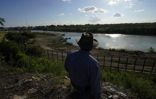 Kayak outfitter Jessie Fuentes stands above the Rio Grande in Eagle Pass , Texas, Thursday, July 6, 2023, where concertina wire lines the banks of the river that has been recently bulldozed. Texas Republican Gov. Greg Abbott has escalated measures to keep migrants from entering the U.S. He's pushing legal boundaries along the border with Mexico to install razor wire, deploy massive buoys on the Rio Grande and bulldozing border islands in the river. (AP Photo/Eric Gay)