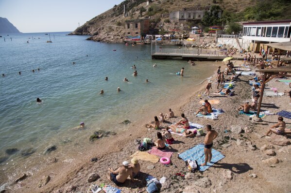 FILE - People gather at the beach area of the Black Sea, in Balaklava's bay, a part of Sevastopol on the Crimean Peninsula on Sunday, Aug. 9, 2015. The Crimean Peninsula's balmy beaches have been vacation spots for Russian czars and has hosted history-shaking meetings of world leaders. And it has been the site of ethnic persecutions, forced deportations and political repression. Now, as Russia’s war in Ukraine enters its 18th month, the Black Sea peninsula is again both a playground and a battleground. (AP Photo, File)