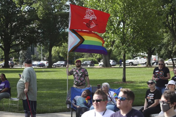 Kirby Evers, a 31-year-old bisexual Lawrence, Kan., resident, displays the red flag of the Democratic Socialists of America and a Pride flag during a rally outside the Kansas Statehouse in favor of transgender rights, Friday, June 30, 2023, in Topeka, Kan. Evers said he believes a U.S. Supreme Court decision allowing a Christian graphic artist to refuse to work with same-sex couples will increase discrimination against LGBTQ people. (AP Photo/John Hanna)