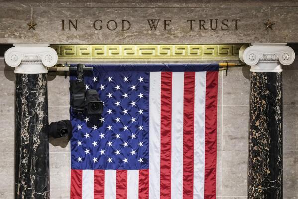 FILE - "In God We Trust" is engraved in stone above a U.S. flag in the House of Representatives chamber at the Capitol in Washington on Tuesday, March 1, 2022. Even though nearly three in 10 Americans claim no religious affiliation — a rate that has steadily risen in recent years — only two of the 534 incoming members of Congress will admit to as much. (Sarahbeth Maney/The New York Times via AP, Pool)