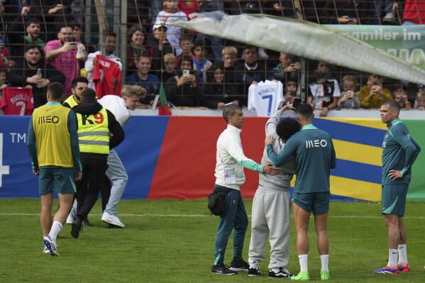 Stewards grab a pitch invader, left, as other pitch invader takes a selfie with Portugal's Cristiano Ronaldo during a training session in Gutersloh, Germany, Friday, June 14, 2024. Portugal will play against Czech Republic during their Group F soccer match at the Euro 2024 soccer tournament on June 18. (AP Photo/Hassan Ammar)