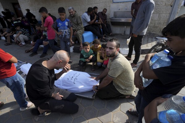 Palestinians mourn over the body of their father, Mohsem al Hegi, who was killed in the Israeli bombardment of the Gaza Strip in front of the morgue of al Aqsa Hospital in Deir al Balah, Gaza Strip, Monday, Nov. 13, 2023. (AP Photo/Adel Hana)
