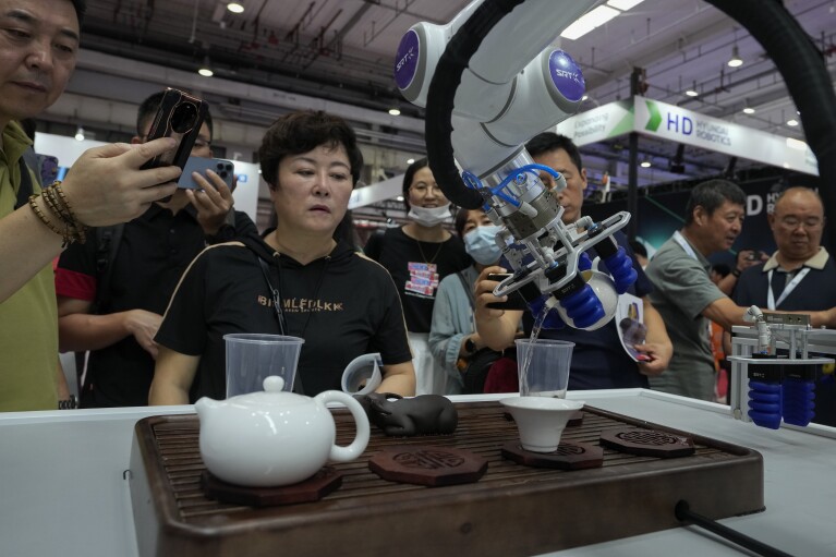 Visitors look at a robotic arm performs a Chinese tea serving during the annual World Robot Conference at the Etrong International Exhibition and Convention Center on the outskirts of Beijing, Thursday, Aug. 17, 2023. (AP Photo/Andy Wong)