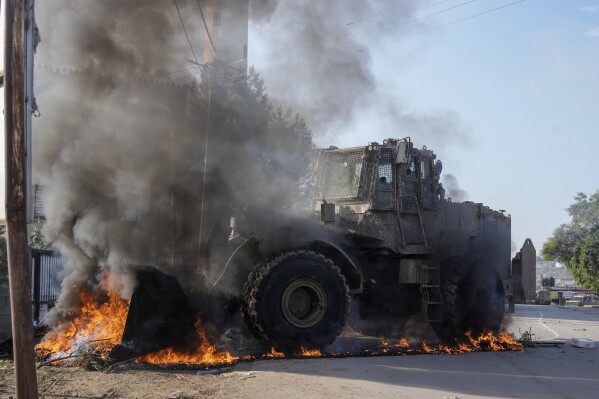 An Israeli army vehicle removes tires blocking roads that Palestinians had set on fire during a military raid into Faraa refugee camp, West Bank, Friday, Dec. 8, 2023. The Palestinian Health Ministry says that five Palestinians were killed when Israeli forces raided the camp prompting fighting with local militants. (APPhoto/Majdi Mohammed)