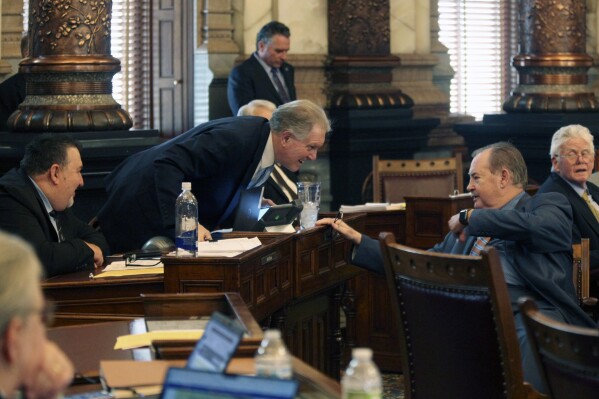 Kansas state Sen. Tim Shallenburger, right, R-Baxter Springs, reaches over to talk to Sen. Mike Thompson, R-Shawnee, during a Senate debate, Thursday, March 14, 2024, at the Statehouse in Topeka, Kan. Republicans are trying to lock in two-thirds majorities in both chambers on a proposed ban on gender-affirming care for minors, so that they can override an expected veto from Democratic Gov. Laura Kelly. (AP Photo/John Hanna)