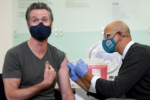 FILE - California Gov. Gavin Newsom, left, receives a Moderna COVID-19 vaccine booster shot from California Health and Human Services Secretary Dr. Mark Ghaly at Asian Health Services in Oakland, Calif., on Oct. 27, 2021. On Monday, Oct. 17, 2022, Newsom announced he will lift the coronavirus state of emergency at the end of February 2023. The announcement will officially end all of the pandemic-related executive orders Newsom has issued since 2020. (AP Photo/Jeff Chiu, File)