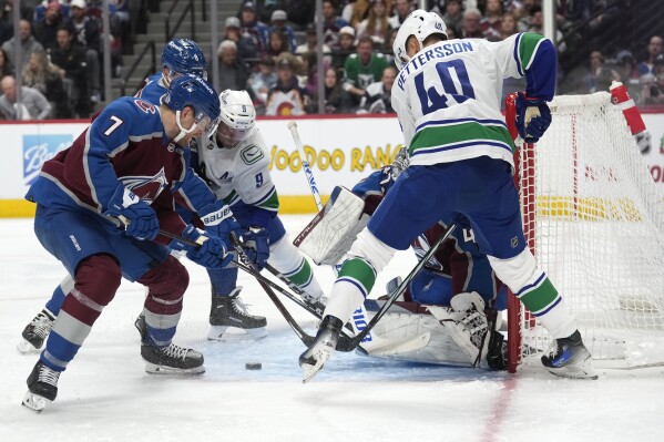Colorado Avalanche defenseman Devon Toews, front left, vie for control of the puck with defenseman Cale Makar and Vancouver Canucks center J.T. Miller, back left, after Avalanche goaltender Alexandar Georgiev,stopped a shot by Vancouver center Elias Pettersson during the second period of an NHL hockey game Wednesday, Nov. 22, 2023, in Denver. (AP Photo/David Zalubowski)
