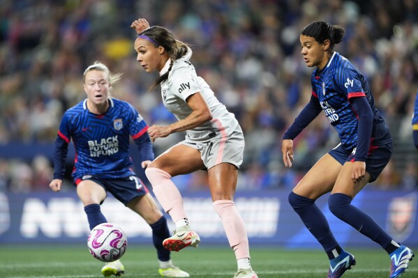 Angel City FC forward Sydney Leroux, center, makes a short pass in front of the goal against OL Reign defender Emily Sonnett, left, and defender Alana Cook, right, during the first half of an NWSL quarterfinal playoff soccer match Friday, Oct. 20, 2023, in Seattle. (AP Photo/Lindsey Wasson)