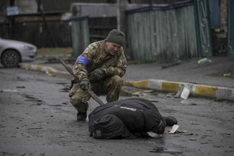 FILE - A Ukrainian serviceman uses a piece of wood to check if the body of a man dressed in civilian clothing is booby-trapped with explosive devices, in the formerly Russian-occupied Kyiv suburb of Bucha, Ukraine, Saturday, April 2, 2022. (AP Photo/Vadim Ghirda)
