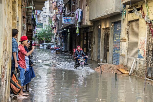 FILE - In this Oct. 25, 2015 file photo, a motorcyclist rides through floodwater in the coastal city of Alexandria, Egypt. Alexandria, which has survived invasions, fires and earthquakes since it was founded by Alexander the Great more than 2,000 years ago, now faces a new menace from climate change. Rising sea levels threaten to inundate poorer neighborhoods and archaeological sites, prompting authorities to erect concrete barriers out at sea to hold back the surging waves. (AP Photo/Heba Khamis, File)