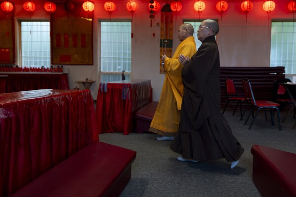 Monk Dauv Singx Si, left, walks towards an altar at the Iu Mien Buddha Light Temple on Tuesday, April 30, 2024, in Gresham, Ore. There is a sizeable Iu Mien community in Portland and its suburbs, with a Buddhist temple and Baptist church, active social organization, and businesses and restaurants. (AP Photo/Jenny Kane)