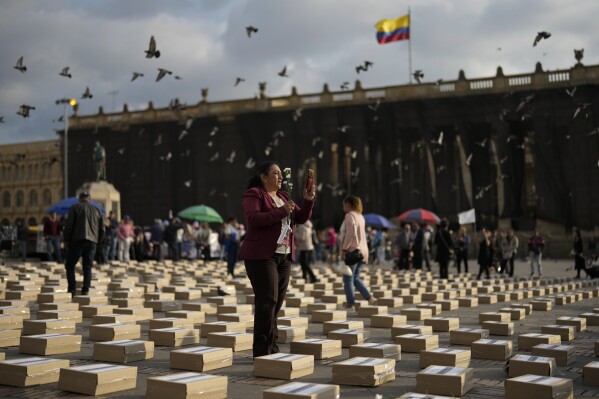 A women stands among boxes representing symbolic coffins as she remembers former guerrillas and social leaders who have been killed since the 2016 signing of a peace agreement between rebels of the Revolutionary Armed Forces of Colombia, FARC, and the government, in Bogota, Colombia, Tuesday, Feb. 20, 2024. (AP Photo/Fernando Vergara)