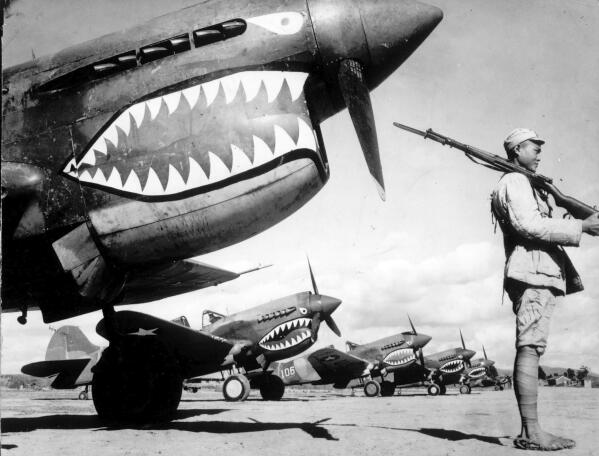 FILE - Guarded by a Chinese soldier, a squadron of Curtiss P-40 fighter planes, decorated with the typical shark face of the famed Flying Tigers, are lined up at an unknown airbase in China in 1943. Veterans, historians and officials from China and the United States celebrated the 80th anniversary of the Flying Tigers, an air unit that delivered aid to Chinese troops fighting the Japanese military occupation during World War II. The meeting on Tuesday, Nov. 16, 2021,  was a reminder of positive historic ties between China and the U.S. on the same day the two countries' leaders spoke after years of rising tensions between the world's largest economies.(AP Photo, File)